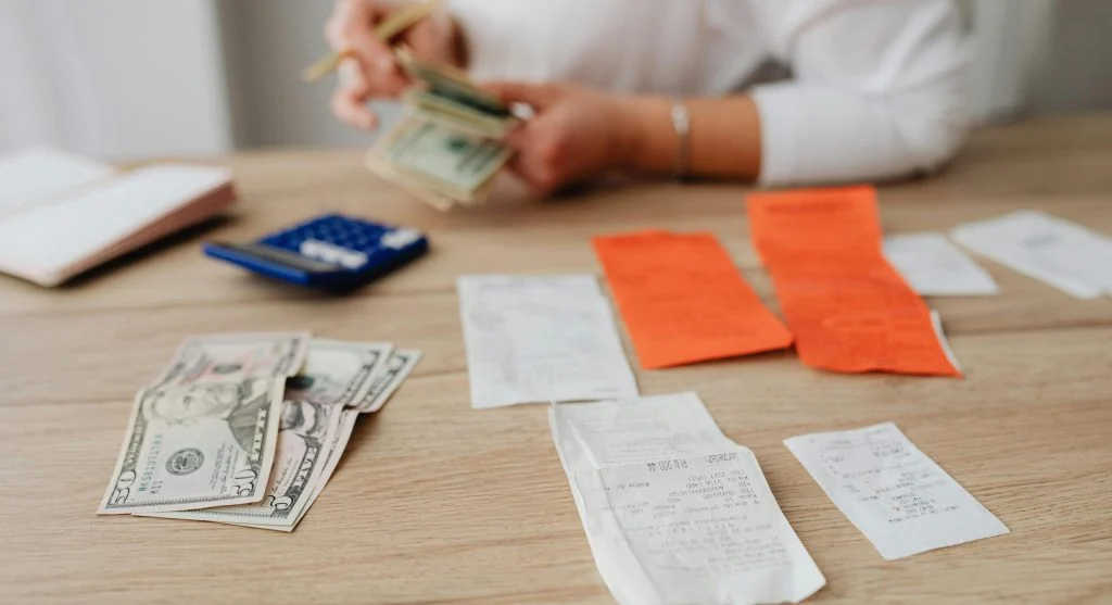 Person sitting at a desk with a laptop and papers, planning a budget