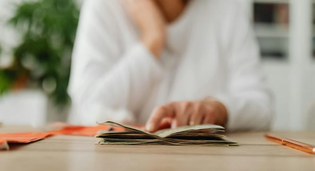 Person sitting at a desk with a budget planner and a laptop, avoiding unnecessary purchases
